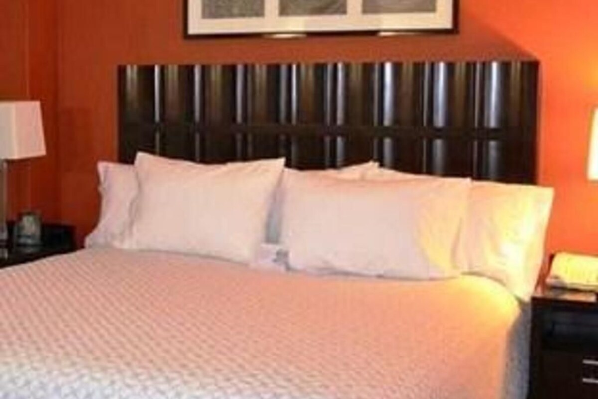A hotel room with a large bed, a headboard, and a framed picture on the wall.