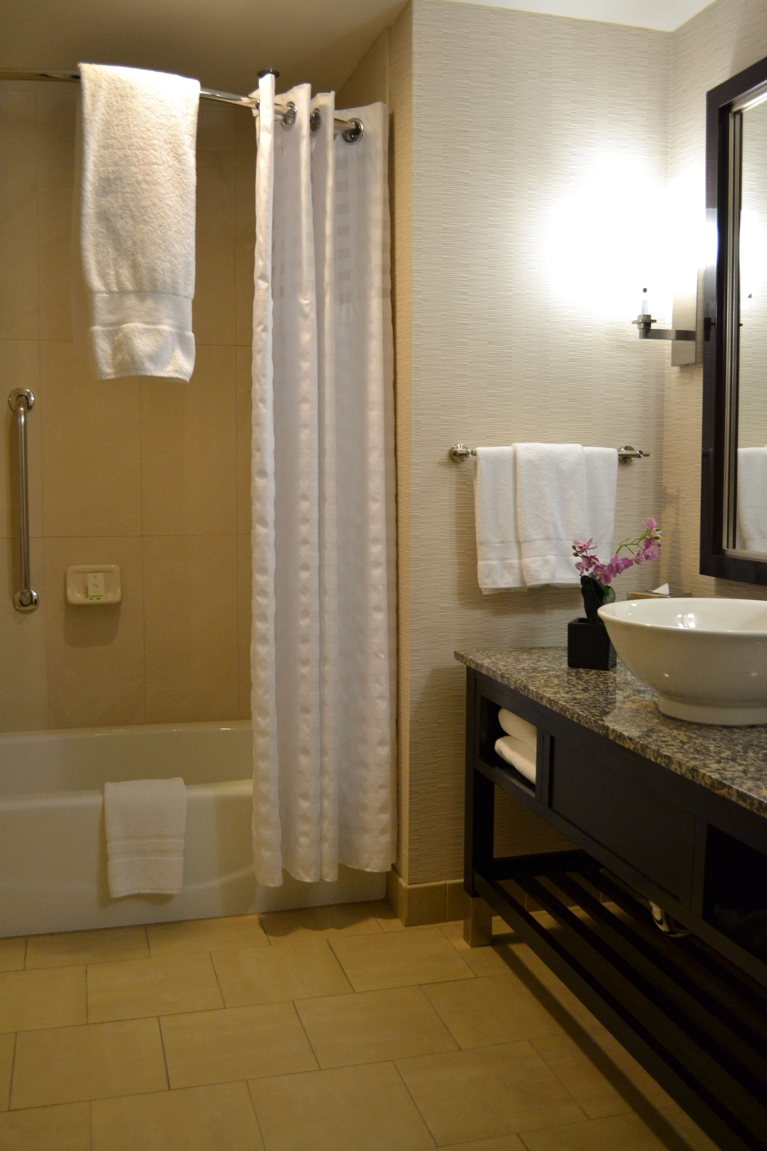 A bathroom with a bathtub, a shower curtain, a sink with a vase of flowers, and a mirror.