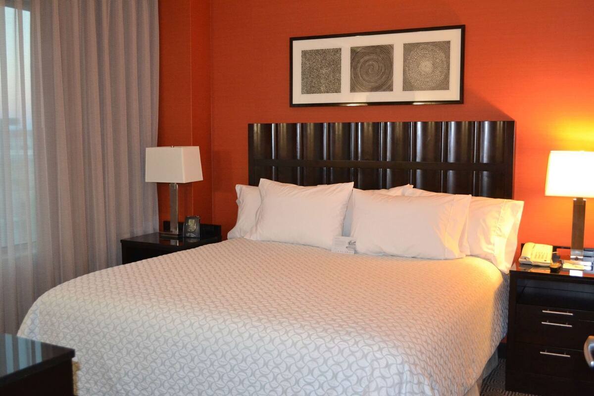 A hotel room with a bed, two bedside tables, a headboard, and a framed artwork above the bed.