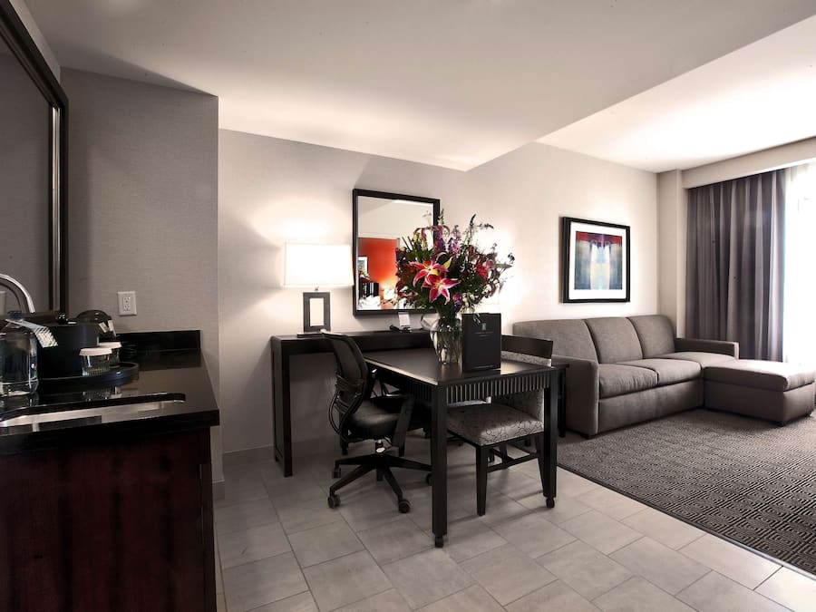 A modern hotel room with a dining area, a sofa, a desk with a chair, and a large mirror.