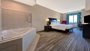 Habitación de hotel con una bañera grande, una cama con ropa blanca, un escritorio con una silla y un televisor.
