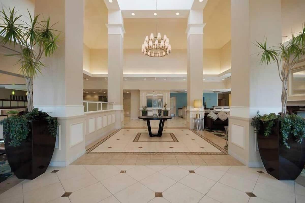 A spacious lobby with a chandelier, large potted plants, and a central table.