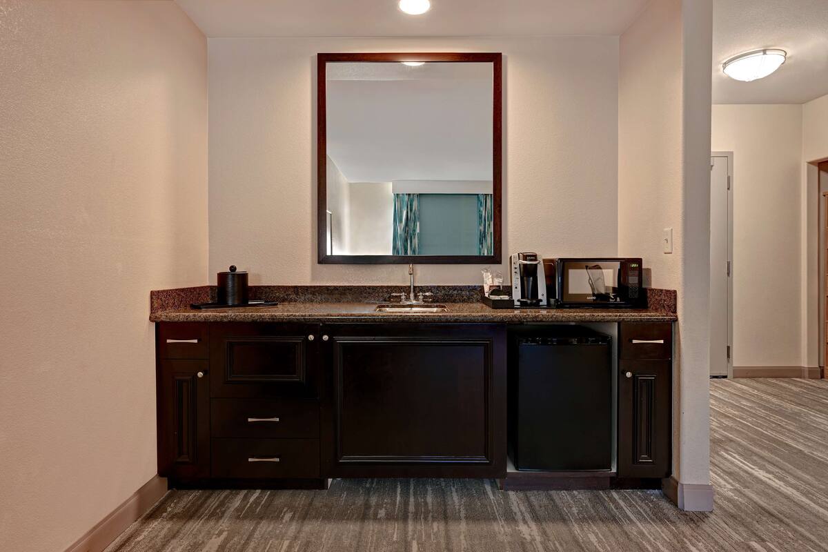 A modern bathroom with a dark wood vanity, a large mirror, and a countertop with a coffee maker and other toiletries.