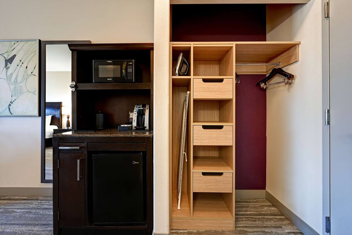 A compact kitchen with a microwave, a refrigerator, and a wooden cabinet with open shelves.