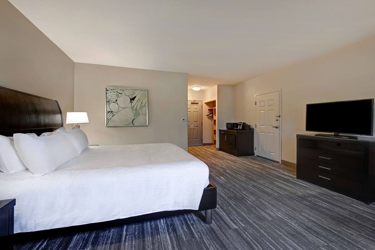 A hotel room with a large bed, a TV, a desk, and a wardrobe.