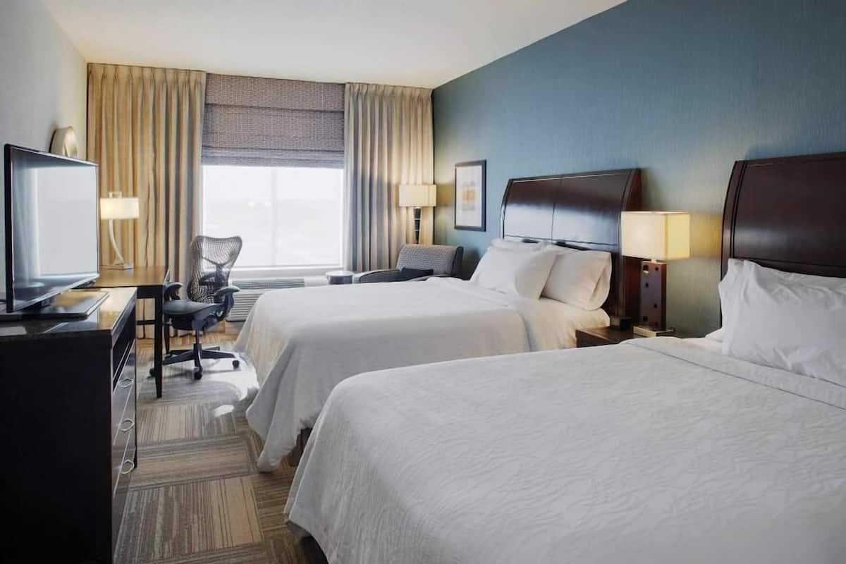A hotel room with two beds, a desk with a computer, a chair, and a television.