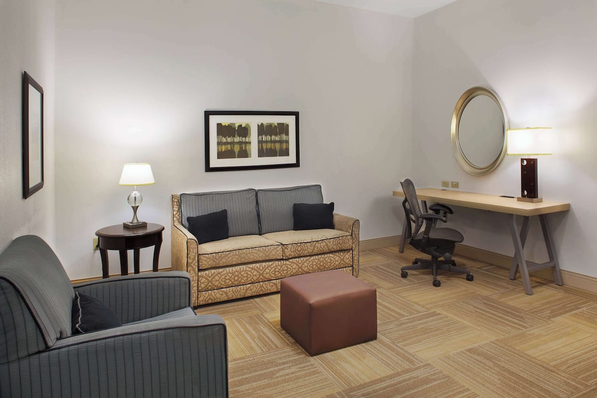 A hotel room with a sofa, a desk, a chair, a small table, and a framed picture on the wall.