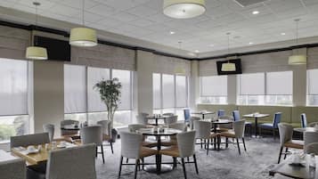 A hotel conference room with round tables, chairs, and a large window offering a view.