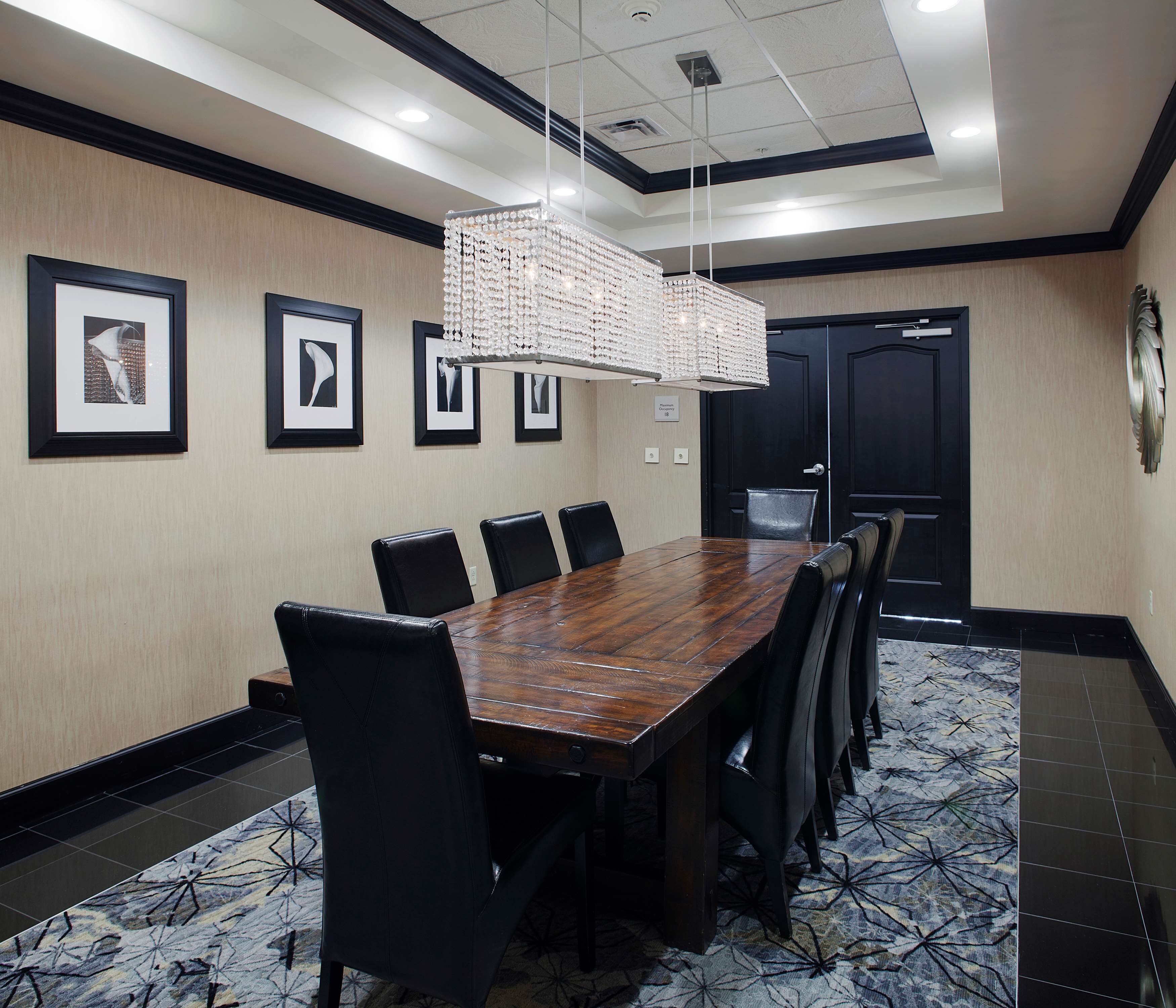 A conference room with a long wooden table, black leather chairs, framed pictures on the wall, and a chandelier.