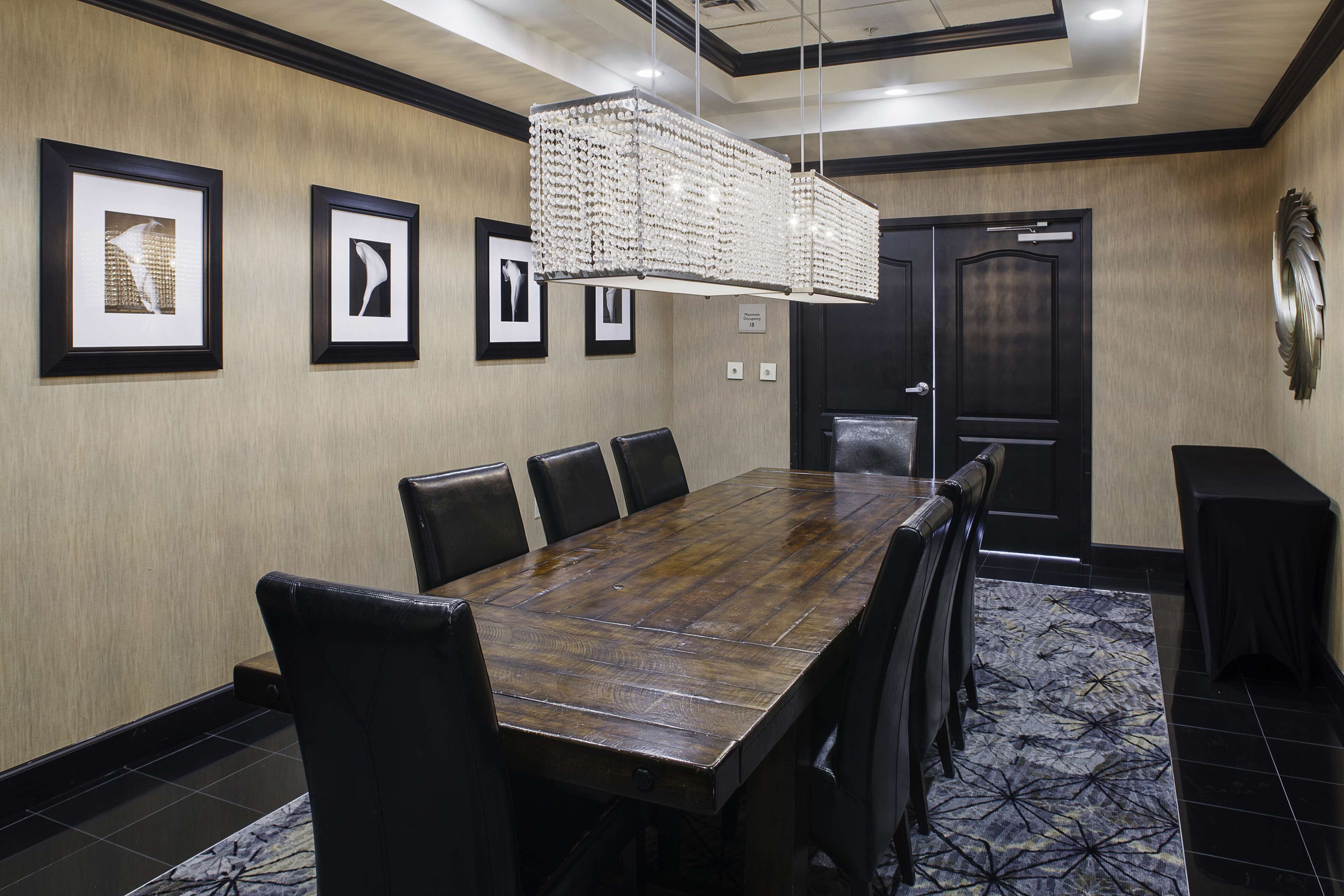 A conference room with a wooden table, black leather chairs, framed artwork on the wall, and a patterned carpet.