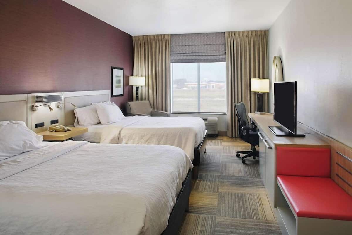 A hotel room with two beds, a desk with a computer, a TV, and a window with curtains.