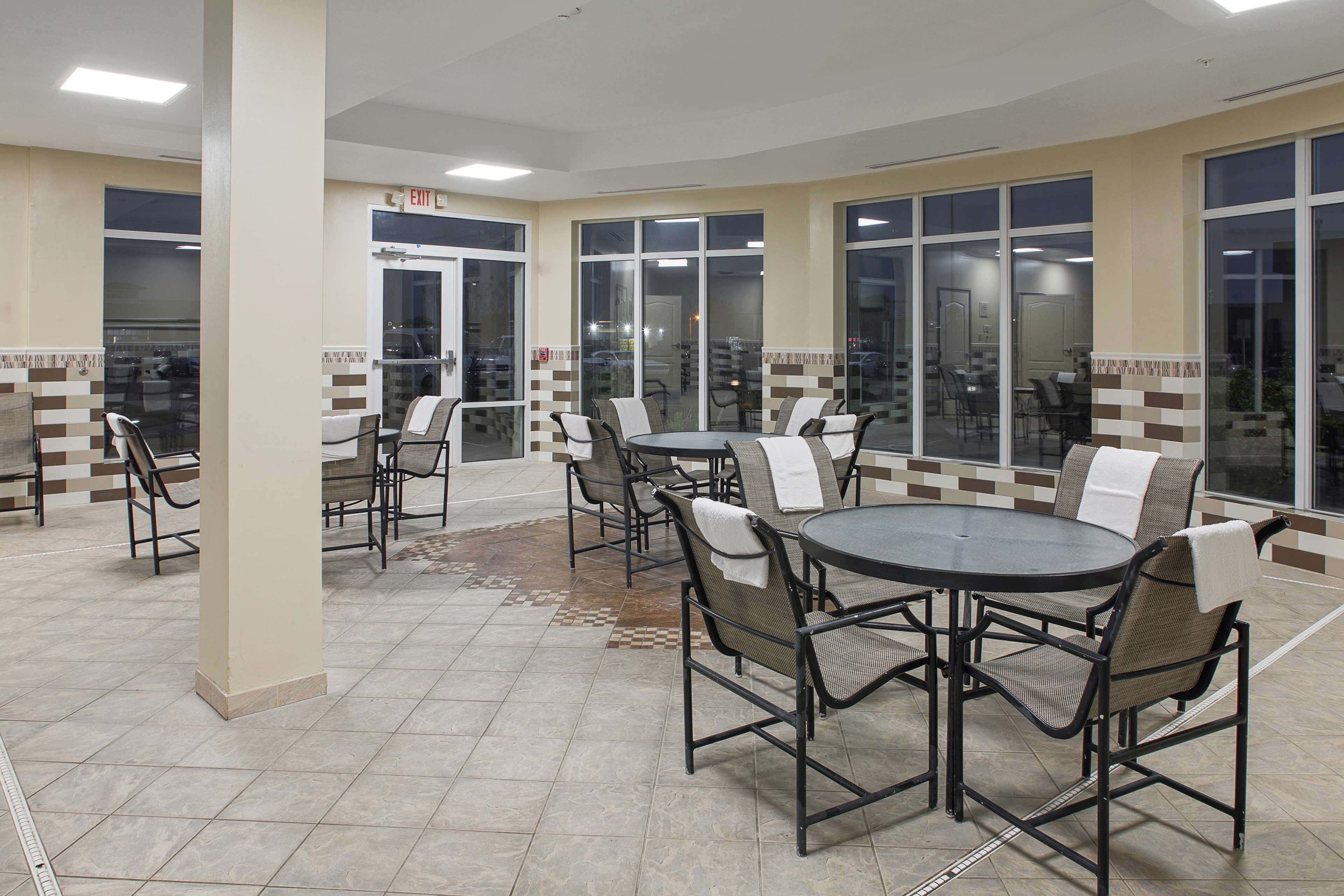 Un patio interior amplio con varias mesas y sillas redondas, ventanas grandes y piso de baldosas.