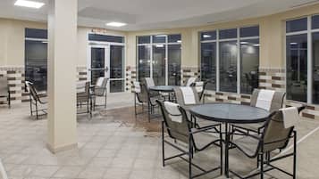 A spacious indoor patio area with multiple round tables and chairs, large windows, and a tiled floor.