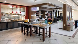 A modern kitchen area with a central island, a buffet setup, and a variety of food items. - Hilton Garden Inn Jonesboro (Jonesboro)