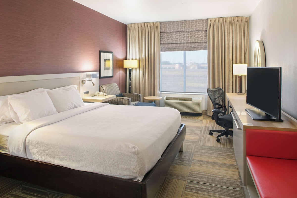 A hotel room with a large bed, a desk with a TV, a chair, a lamp, and a window with curtains.