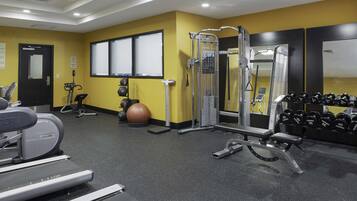 Un gimnasio con equipo de ejercicio, una cinta de correr y un espejo montado en la pared.