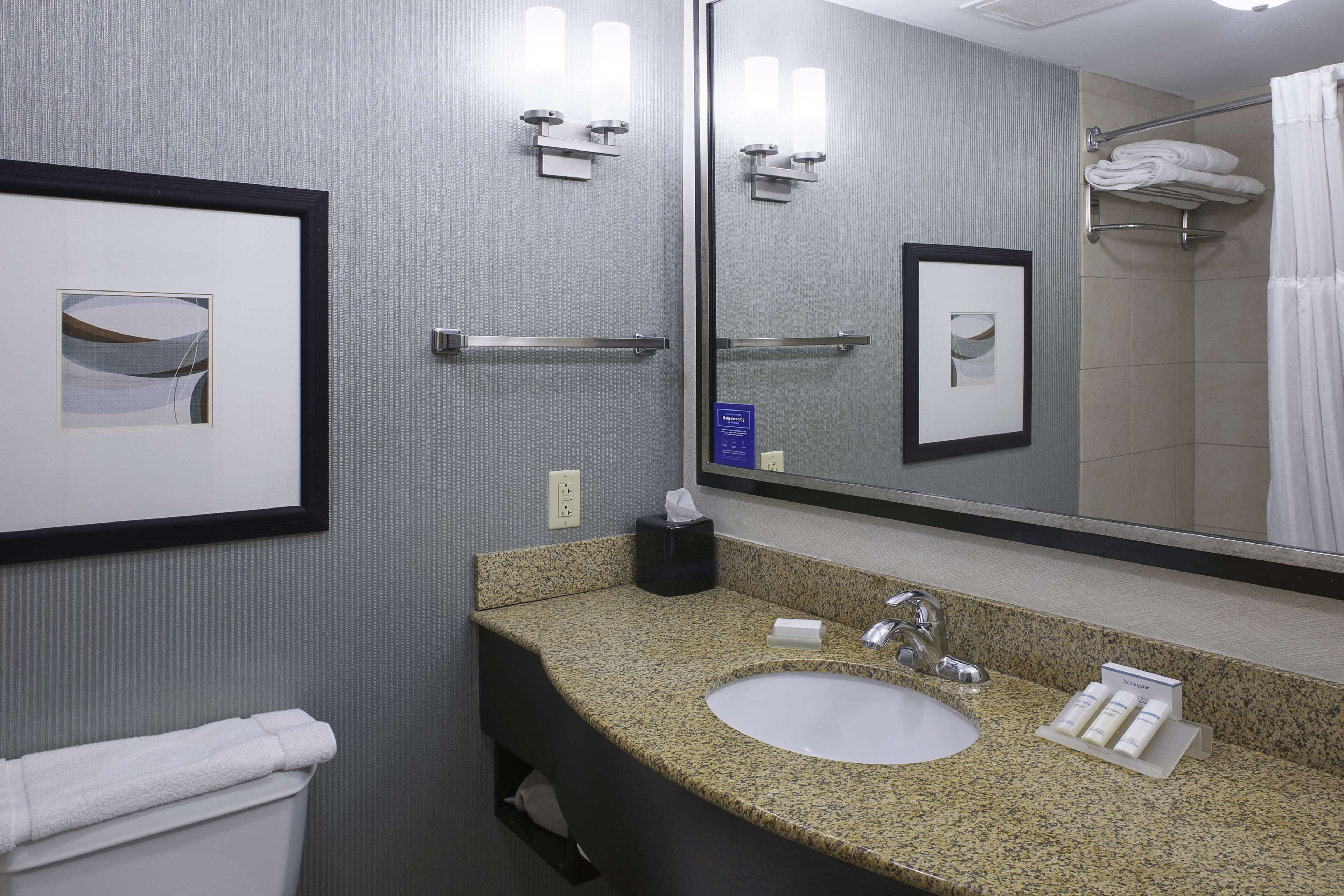 A bathroom with a granite countertop sink, a mirror, framed pictures, and a towel rack with folded towels.