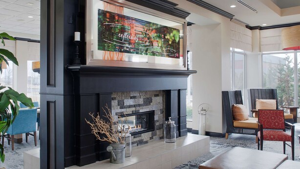 A modern living room with a fireplace, a large TV mounted above it, and comfortable seating. - Hilton Garden Inn Jonesboro (Jonesboro)