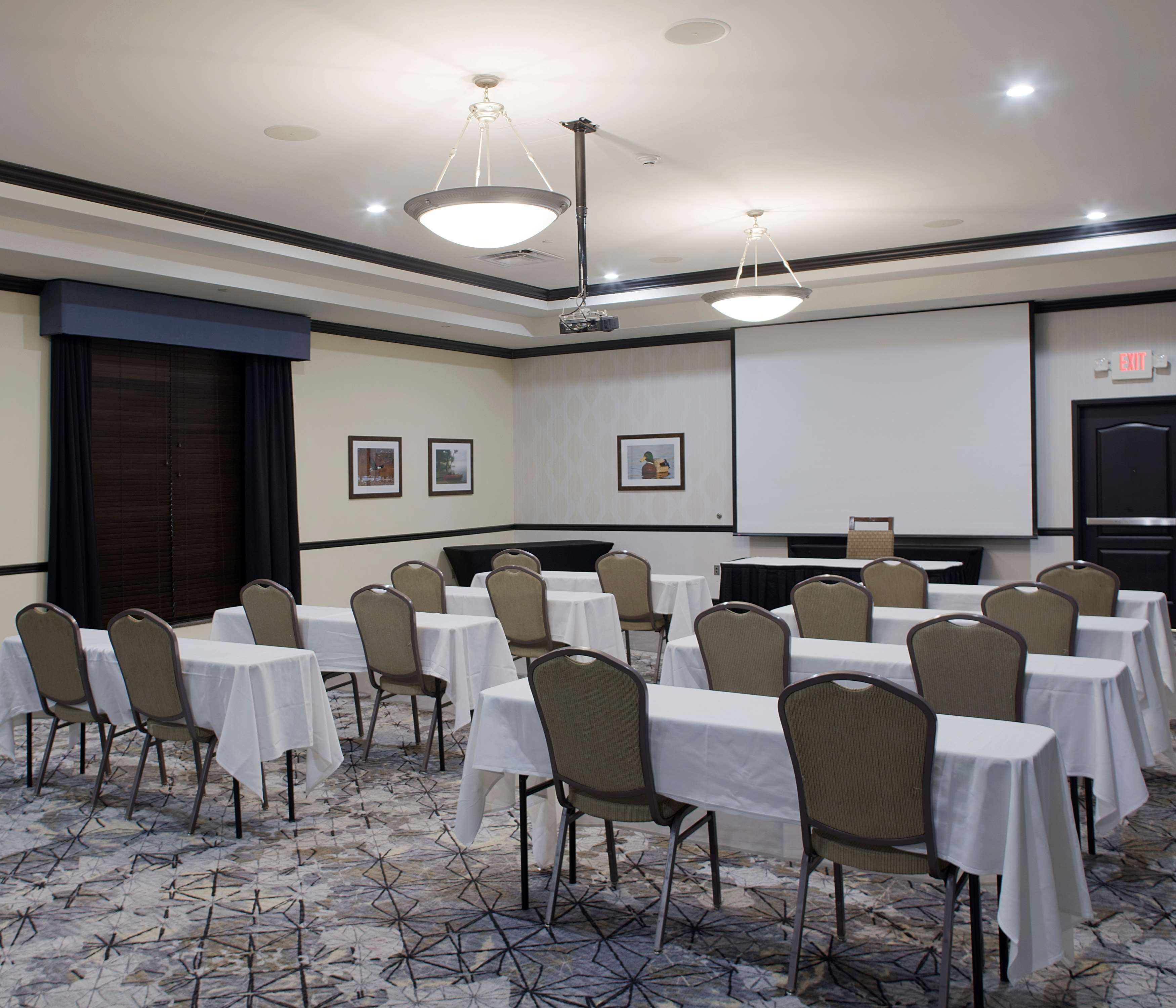 A conference room with tables and chairs, a projector screen, and framed pictures on the wall.