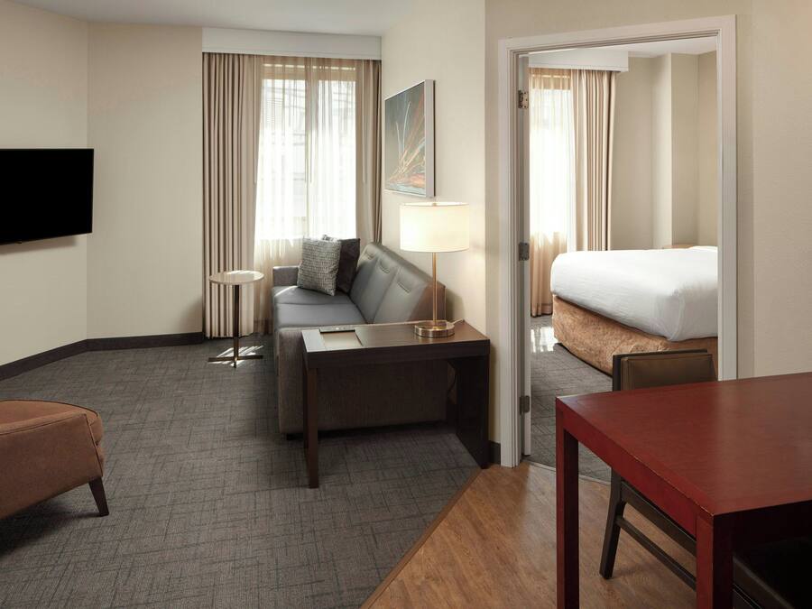 A hotel room with a sofa, a desk, a TV, a bed, and a table.