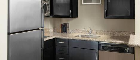 A modern kitchen with black cabinets, stainless steel appliances, a granite countertop, and a wooden dining table.