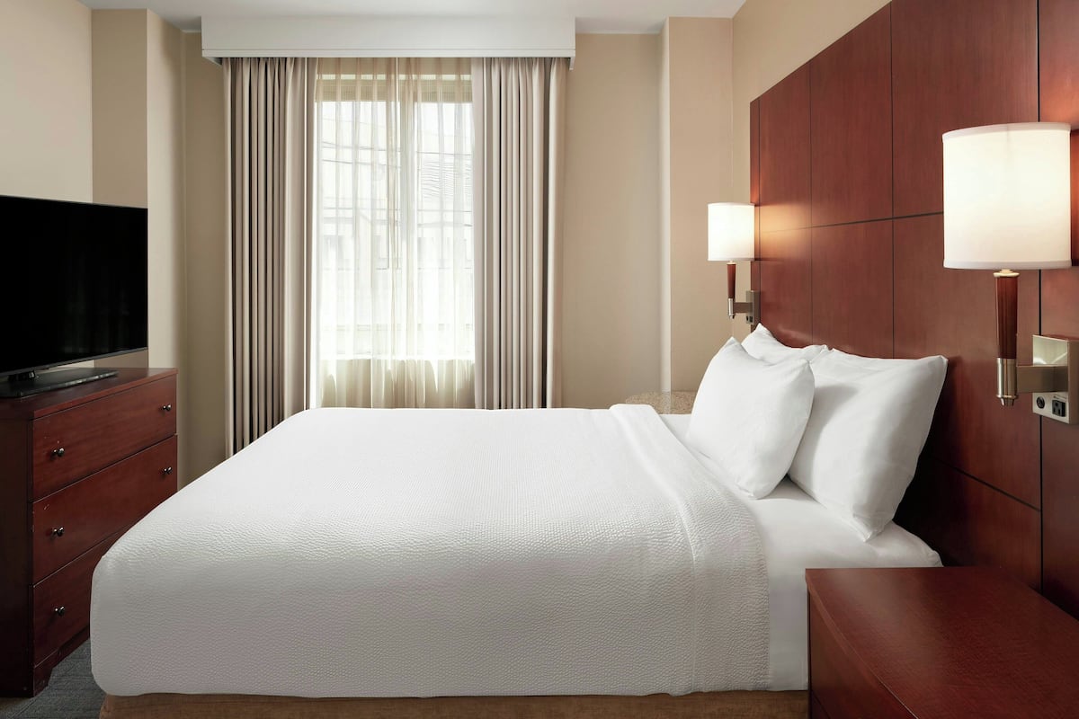 Une chambre d’hôtel avec un grand lit, un téléviseur à écran plat, une commode en bois et une fenêtre avec des rideaux.