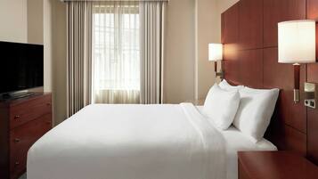 A hotel room with a large bed, a flat-screen TV, a wooden dresser, and a window with curtains.