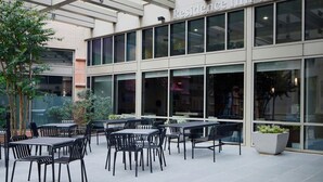 Un hôtel moderne avec une façade contemporaine, un espace extérieur abrité avec des sièges et une vue dégagée sur l’enseigne de l’établissement.