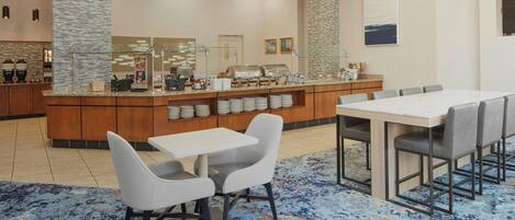 A hotel lobby with a buffet area, seating arrangements, and a stone accent wall.