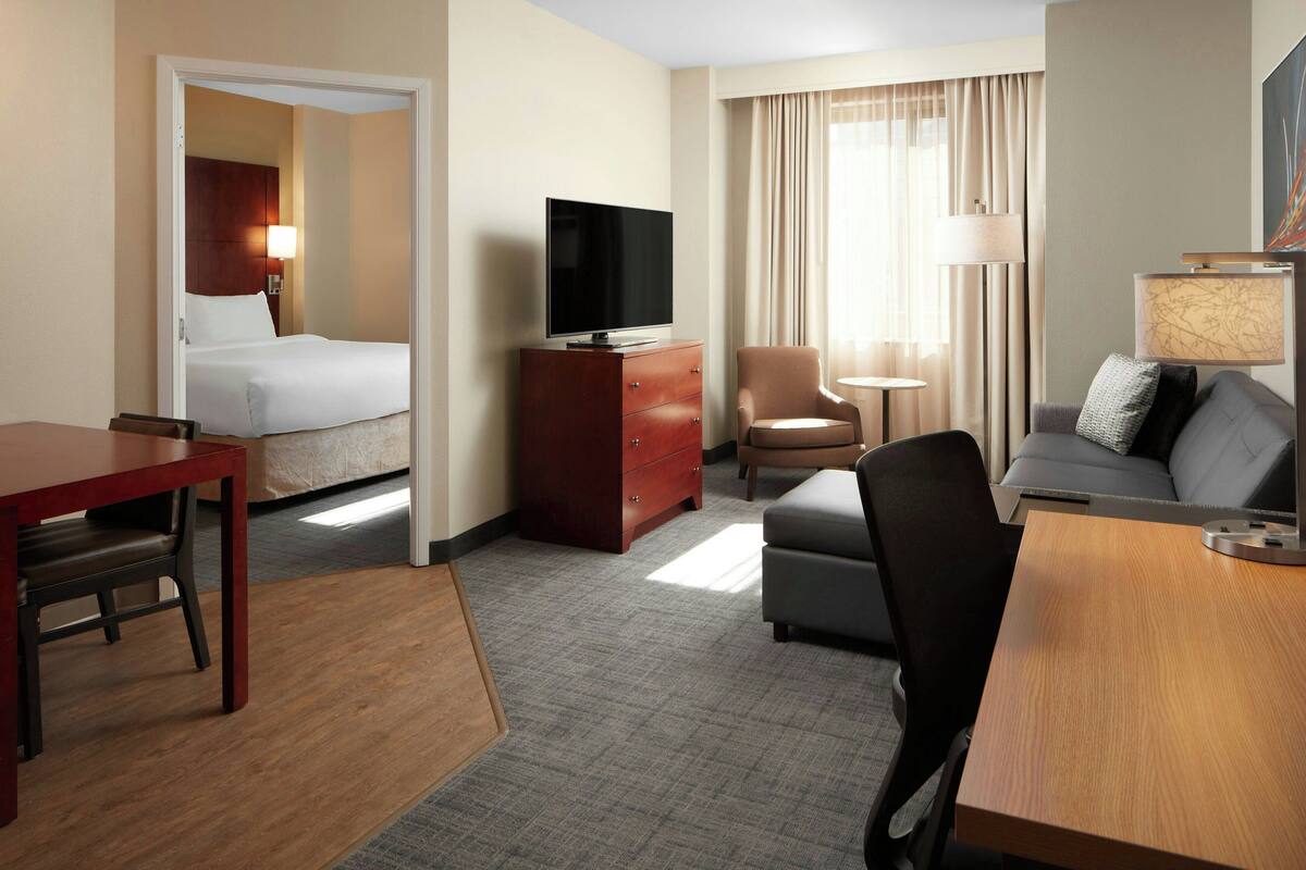 Une chambre d’hôtel avec un lit, un téléviseur posé sur une commode en bois, un canapé, une petite table et une lampe.