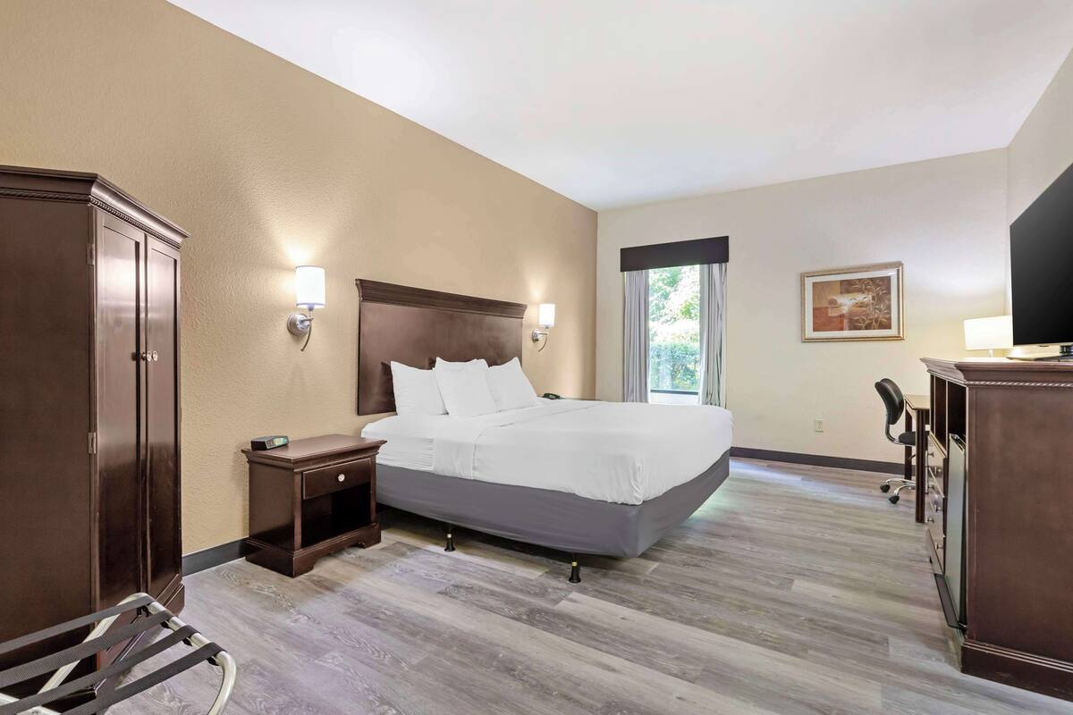 Une chambre d’hôtel avec un grand lit, une armoire en bois, des tables de chevet, un bureau et une chaise.