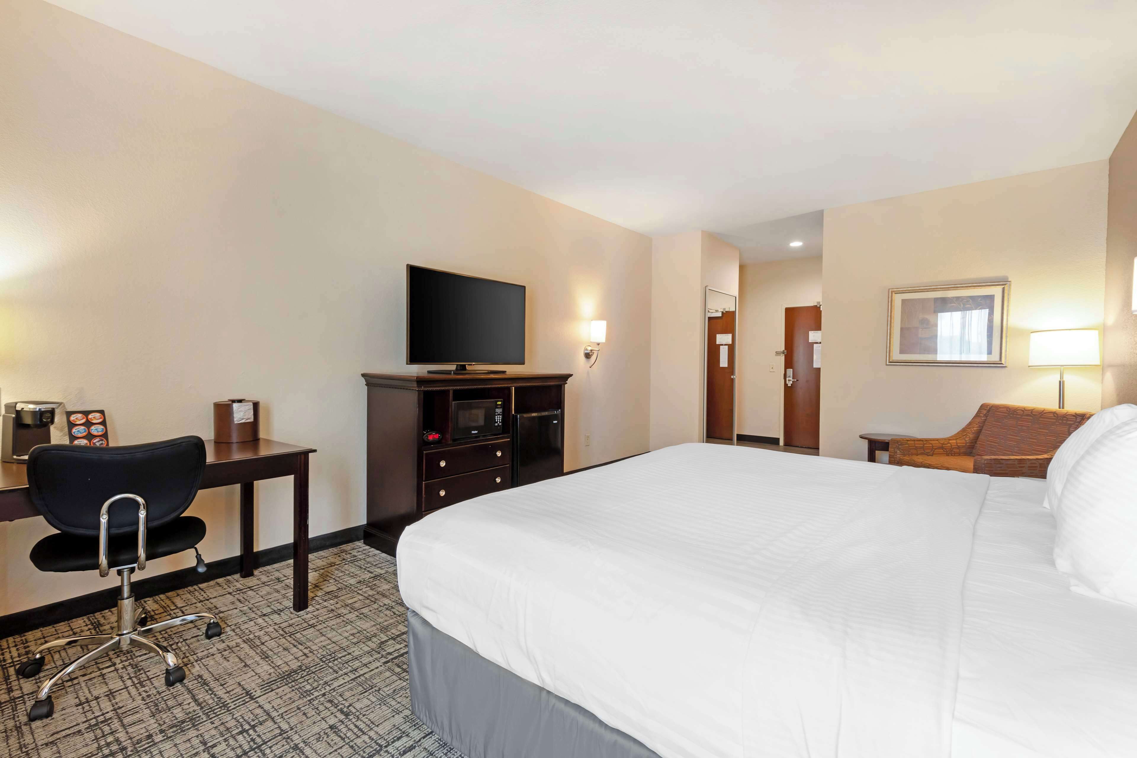 A hotel room with a bed, a desk with a chair, a television, a dresser, and a lamp.