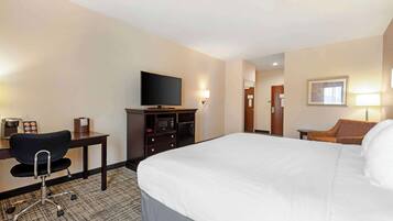 A hotel room with a bed, a desk with a chair, a television, a dresser, and a lamp.
