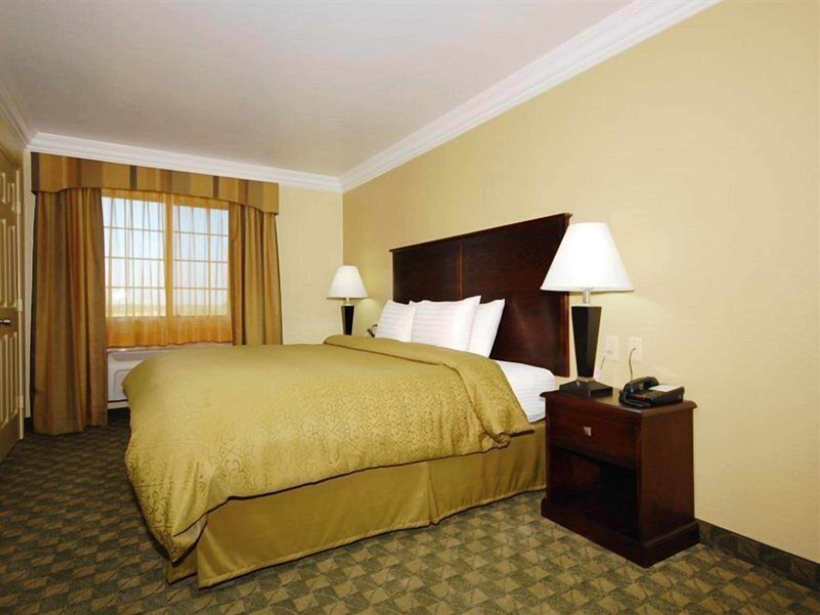 A hotel room with a large bed, two bedside lamps, a nightstand, and a window with curtains.