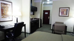 Een hotelkamer met een bed, bureau, stoel, kitchenette en een deur naar een andere kamer.