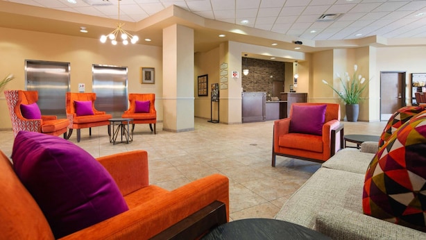 A lobby with orange armchairs, a sofa, a reception desk, and a kitchen area. - Radisson Hotel River Falls (River Falls)