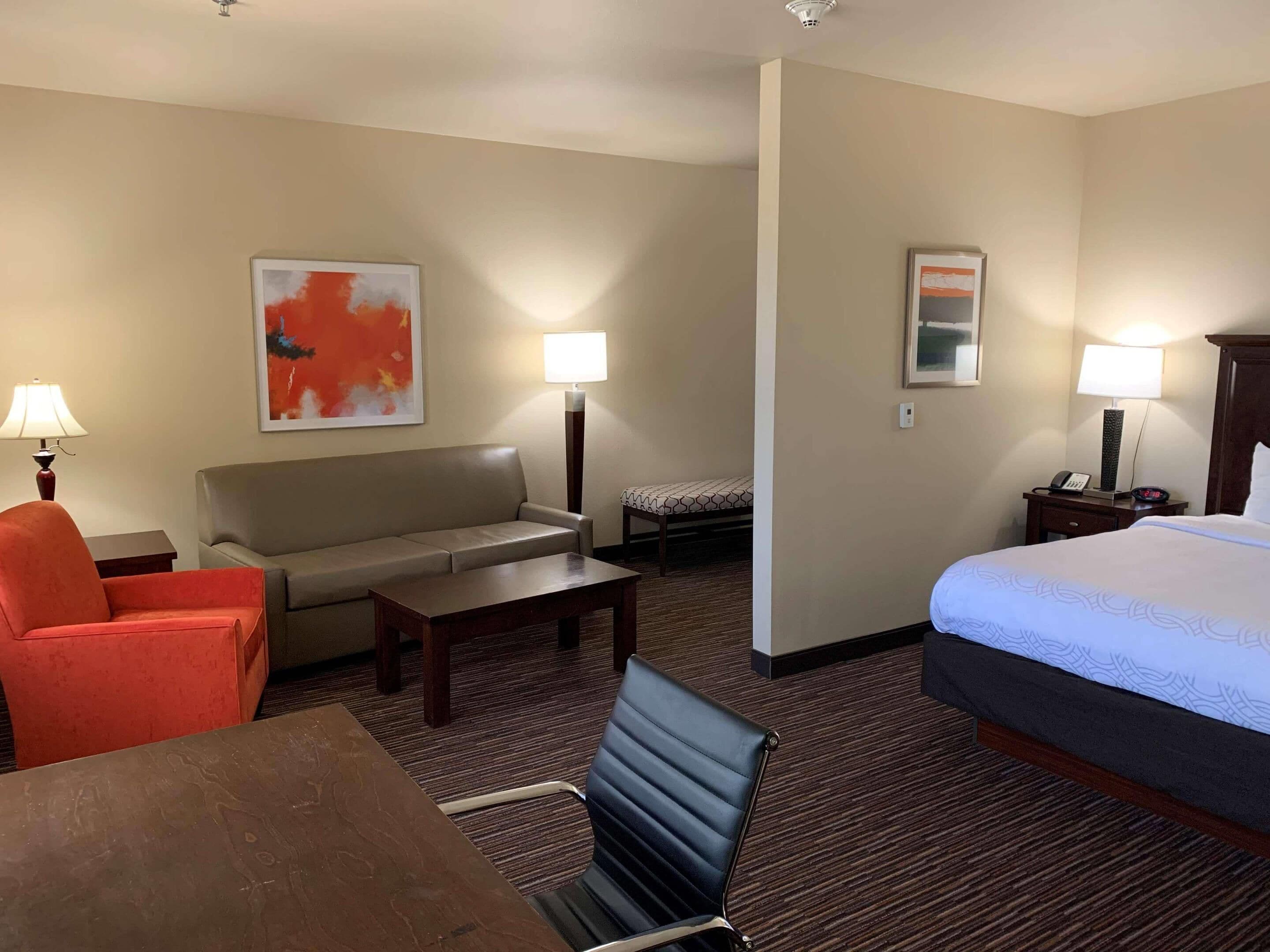Habitación de hotel con cama, sofá, escritorio, silla y dos lámparas.