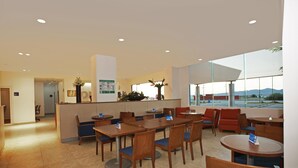 En modern hotellobby med en receptionsdisk, en sittgrupp med bord och stolar samt stora fönster som erbjuder utsikt över omgivningarna.