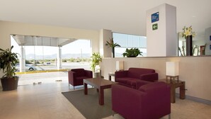 En hotellobby med en receptionsdisk, en sittgrupp och utsikt över parkeringsplatsen.
