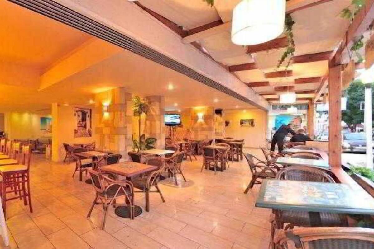 A restaurant with wooden tables and chairs, a bar area, and hanging lights.