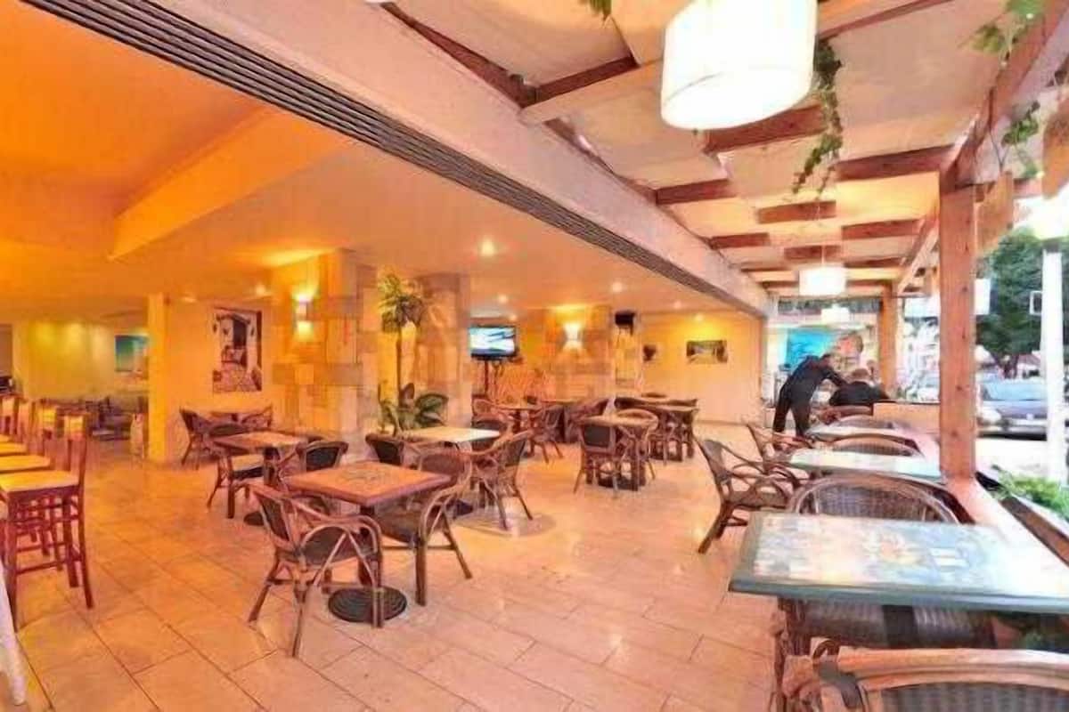 An indoor restaurant with wooden tables and chairs, a bar area, and hanging lights.
