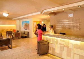 A hotel lobby with a reception desk, seating area, and a wall-mounted information board. - Carina Hotel Rhodes (Rhodes)