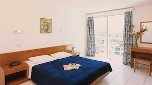 A hotel room with a large bed, a bedside table with a lamp, a desk with a chair, and a window with curtains. - Carina Hotel Rhodes (Rhodes)