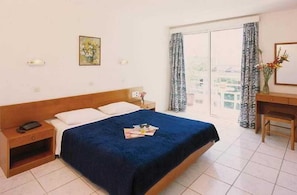 A hotel room with a large bed, a bedside table with a lamp, a desk with a chair, and a window with curtains. - Carina Hotel Rhodes (Rhodes)