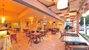 A restaurant with wooden tables and chairs, a bar area, and hanging lights. - Carina Hotel Rhodes (Rhodes)