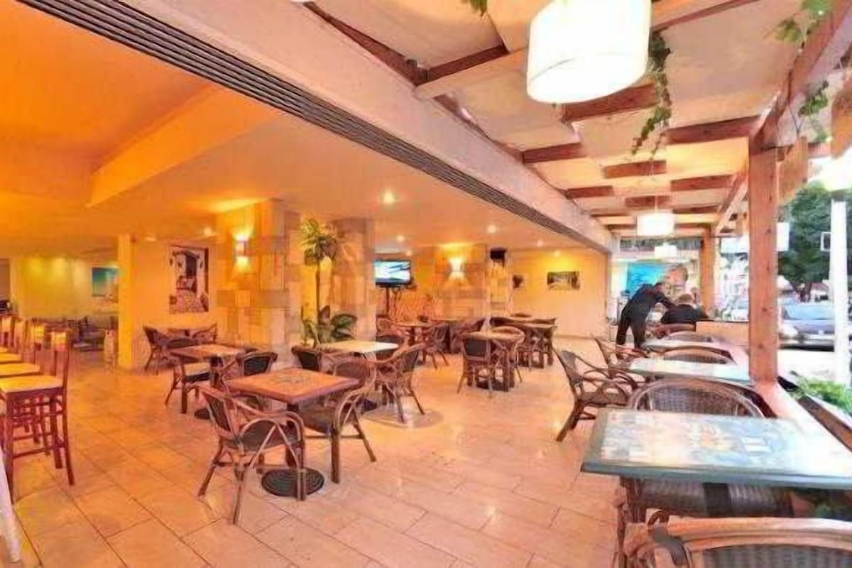 A restaurant with wooden tables and chairs, a bar area, and hanging lights.