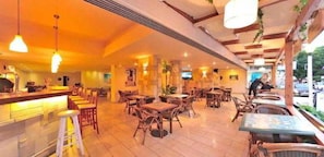 A restaurant with wooden tables and chairs, a bar area, and hanging lights. - Carina Hotel Rhodes (Rhodes)