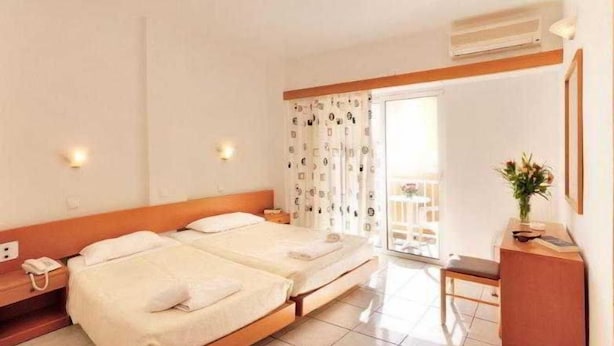 A hotel room with two beds, a desk, a chair, a phone, and a plant. - Carina Hotel Rhodes (Rhodes)
