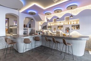A modern bar area with a curved counter, bar stools, and a well-stocked shelf with bottles. - Noufara Hotel (Rhodes)
