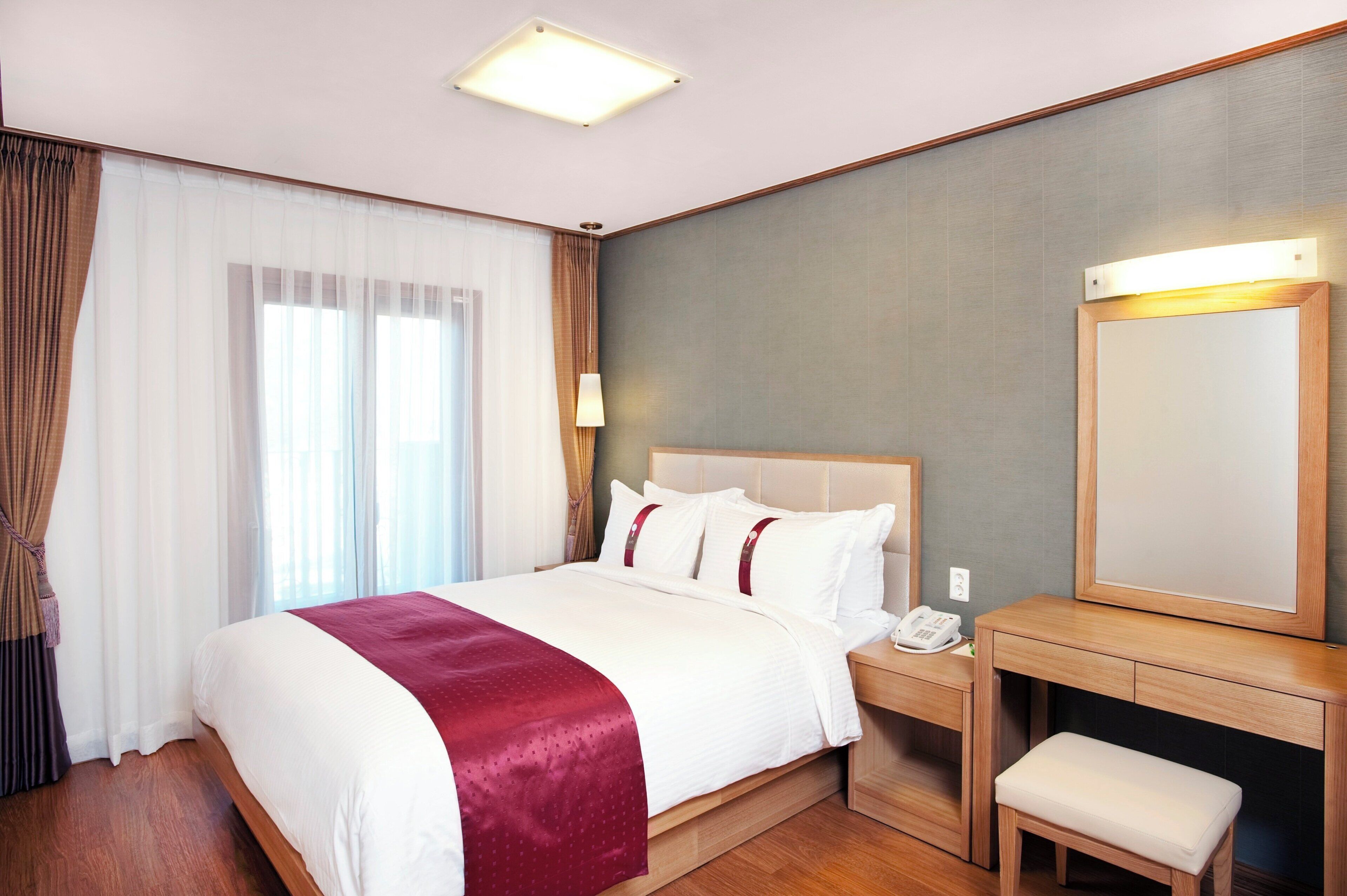 Habitación de hotel con cama, mesita de noche, silla y un espejo grande.